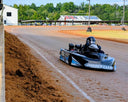 Go-kart on a dirt track with a building and trees in the background